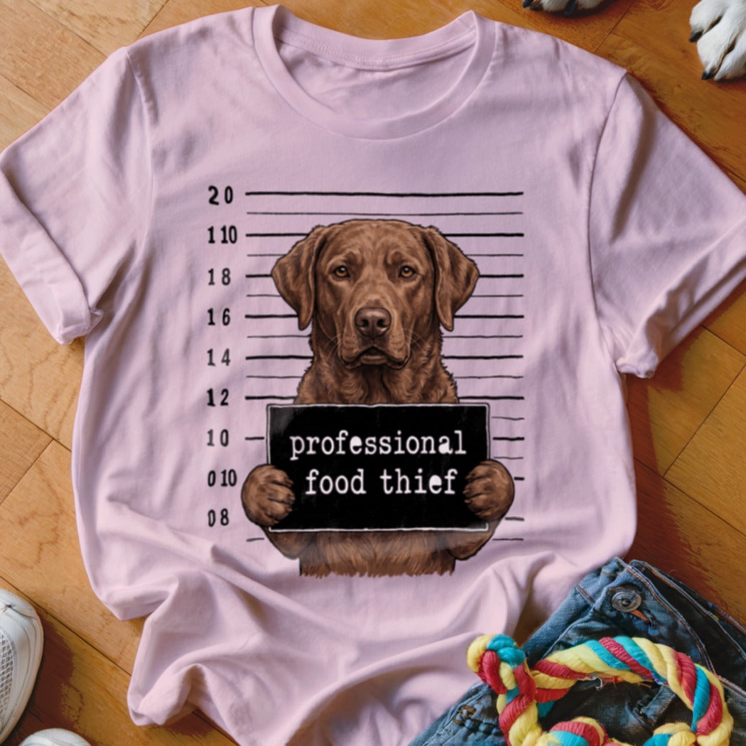 Labrador retriever mugshot with "professional food thief" sign on a pink t-shirt.