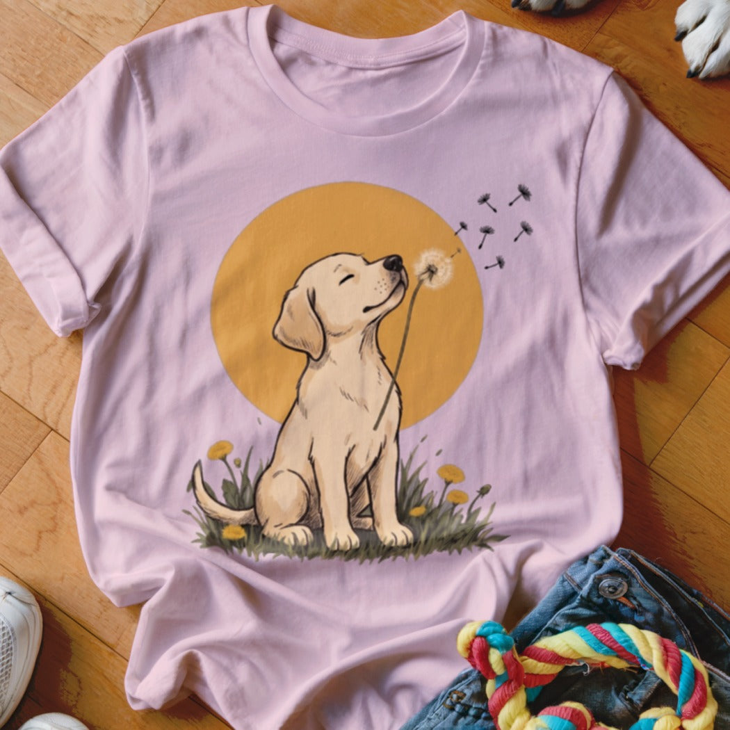 Light pink t-shirt featuring a cartoon illustration of a golden retriever puppy blowing dandelion seeds.