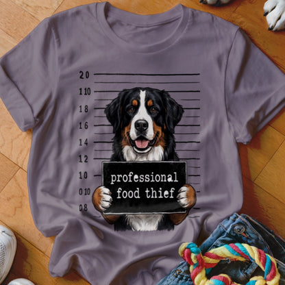 Bernese Mountain Dog mugshot with "professional food thief" sign on a t-shirt.