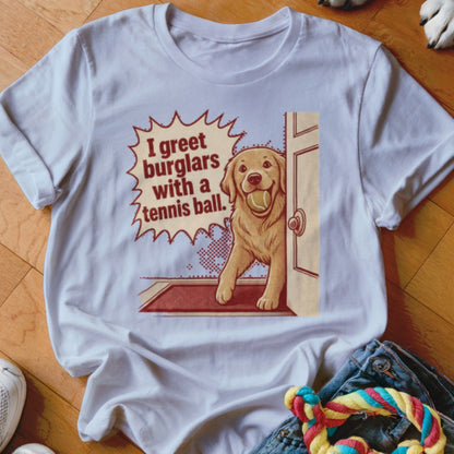 White t-shirt with cartoon of golden retriever holding tennis ball saying "I greet burglars with a tennis ball."