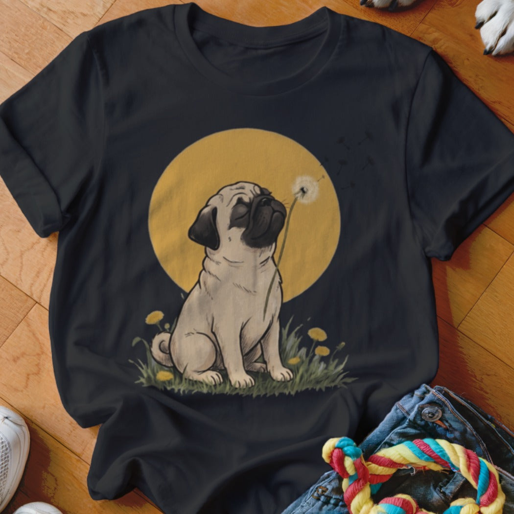 A black short-sleeved t-shirt featuring a graphic of a pug sitting in grass blowing a dandelion against a yellow circle background.