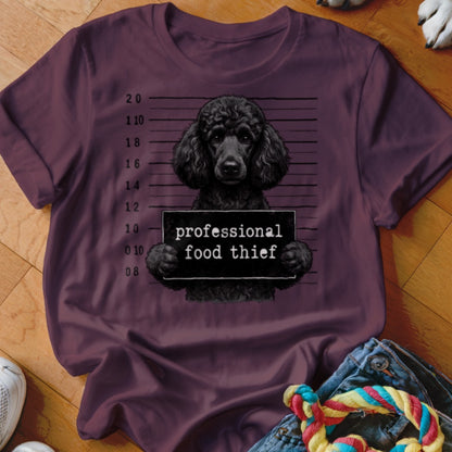 Black poodle mugshot with "professional food thief" sign on maroon t-shirt.