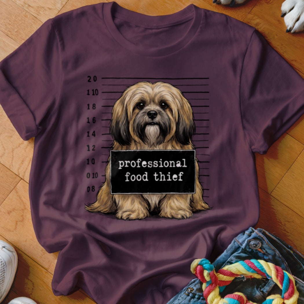 Shih Tzu dog mugshot with "professional food thief" sign on a plum t-shirt.