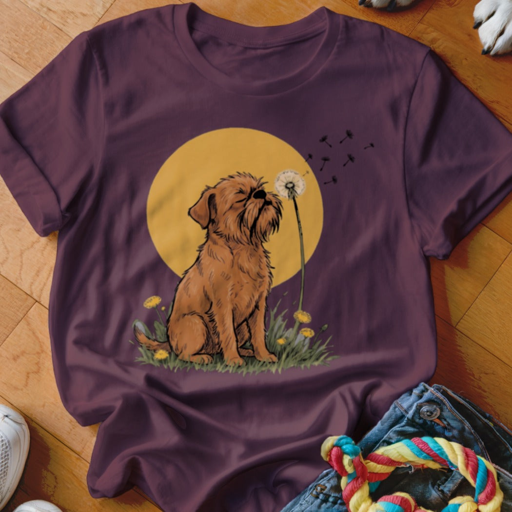 A dark purple t-shirt features a graphic of a small brown dog sitting before a yellow sun and blowing dandelion seeds.
