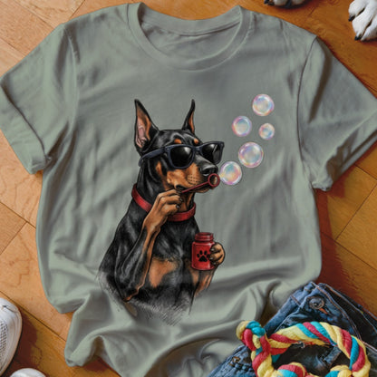 Sage green t-shirt featuring a Doberman wearing sunglasses, blowing soap bubbles from a red bottle.