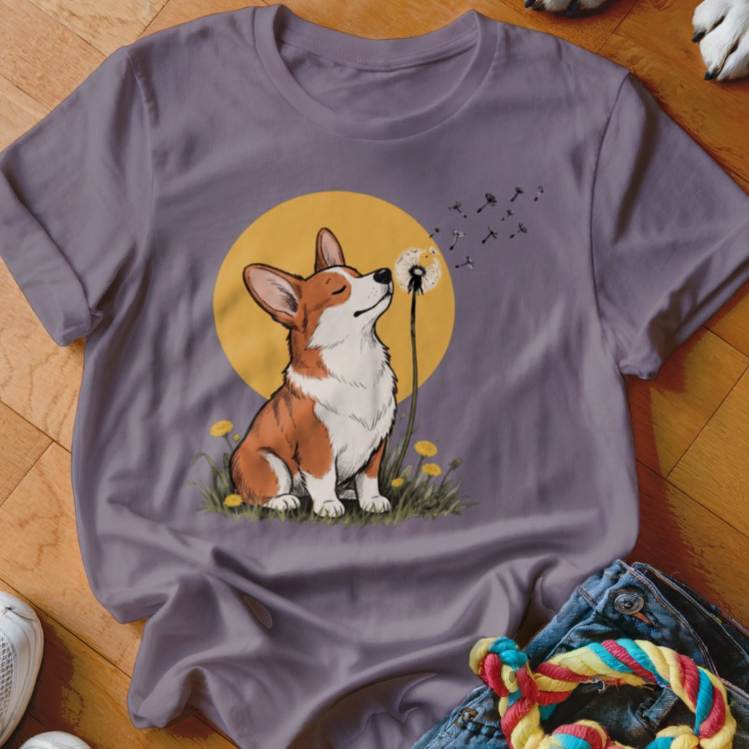 A purple short-sleeve t-shirt with a graphic of a corgi blowing dandelion seeds against a yellow circle background.