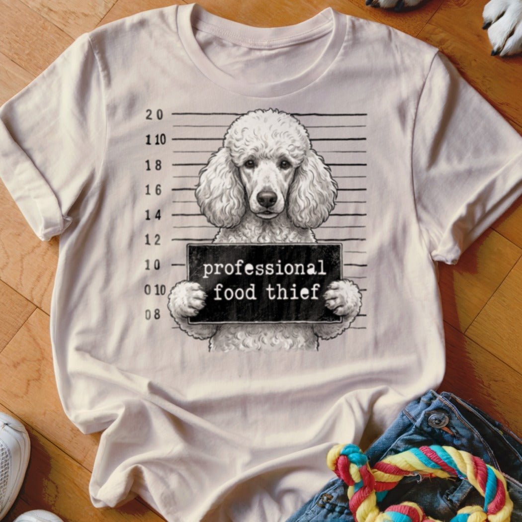 Poodle in mugshot holding "professional food thief" sign on a t-shirt.