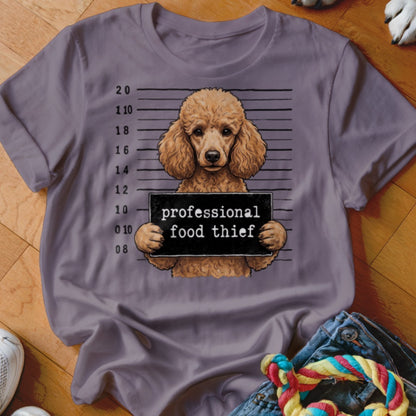 Poodle with mugshot sign reading "professional food thief" on a purple t-shirt.
