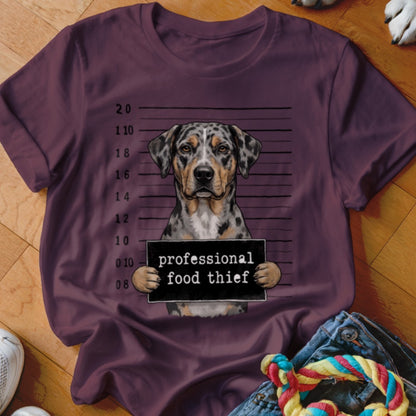Merle dog in mugshot holding "professional food thief" sign.