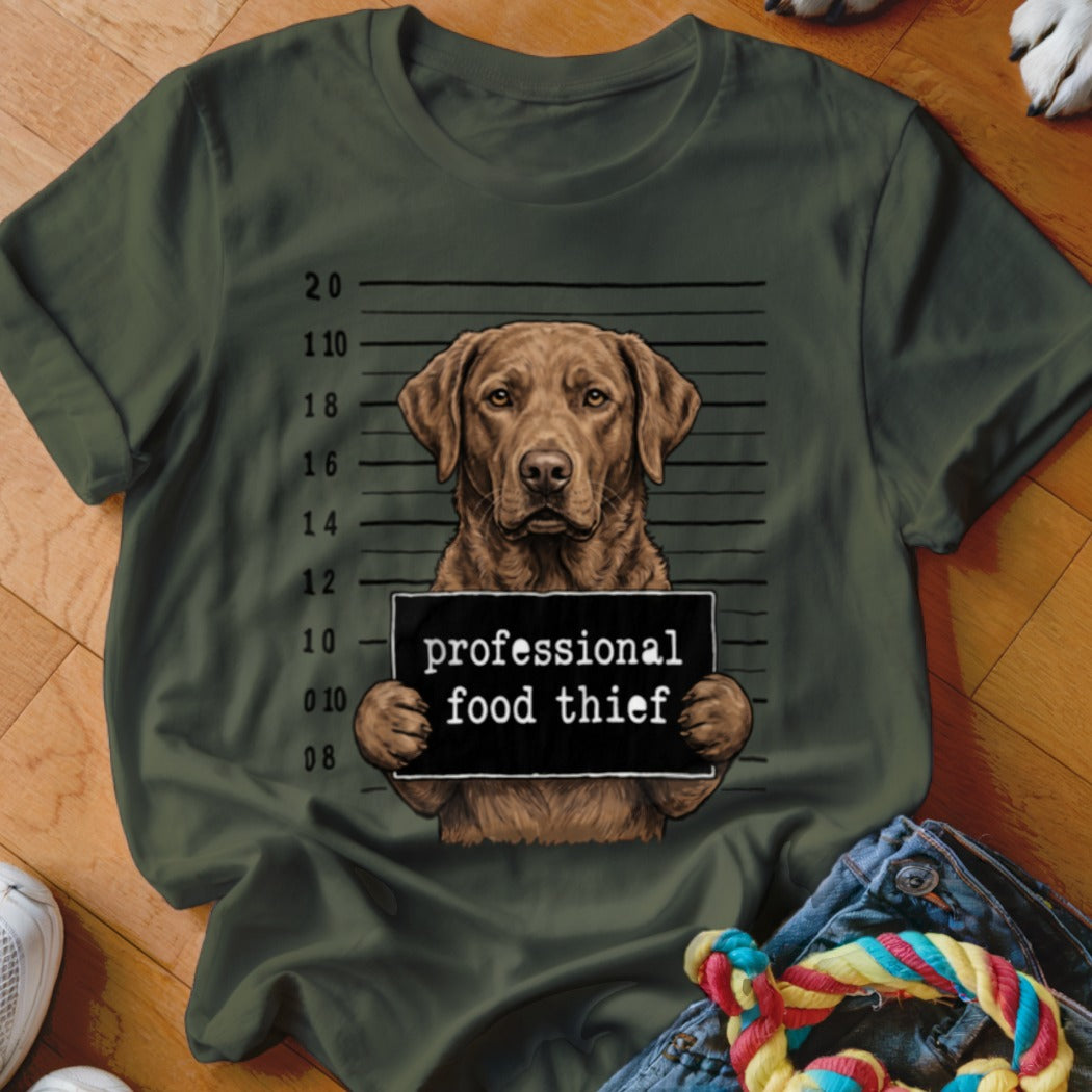 Brown dog in a mugshot holding a sign that says "professional food thief."