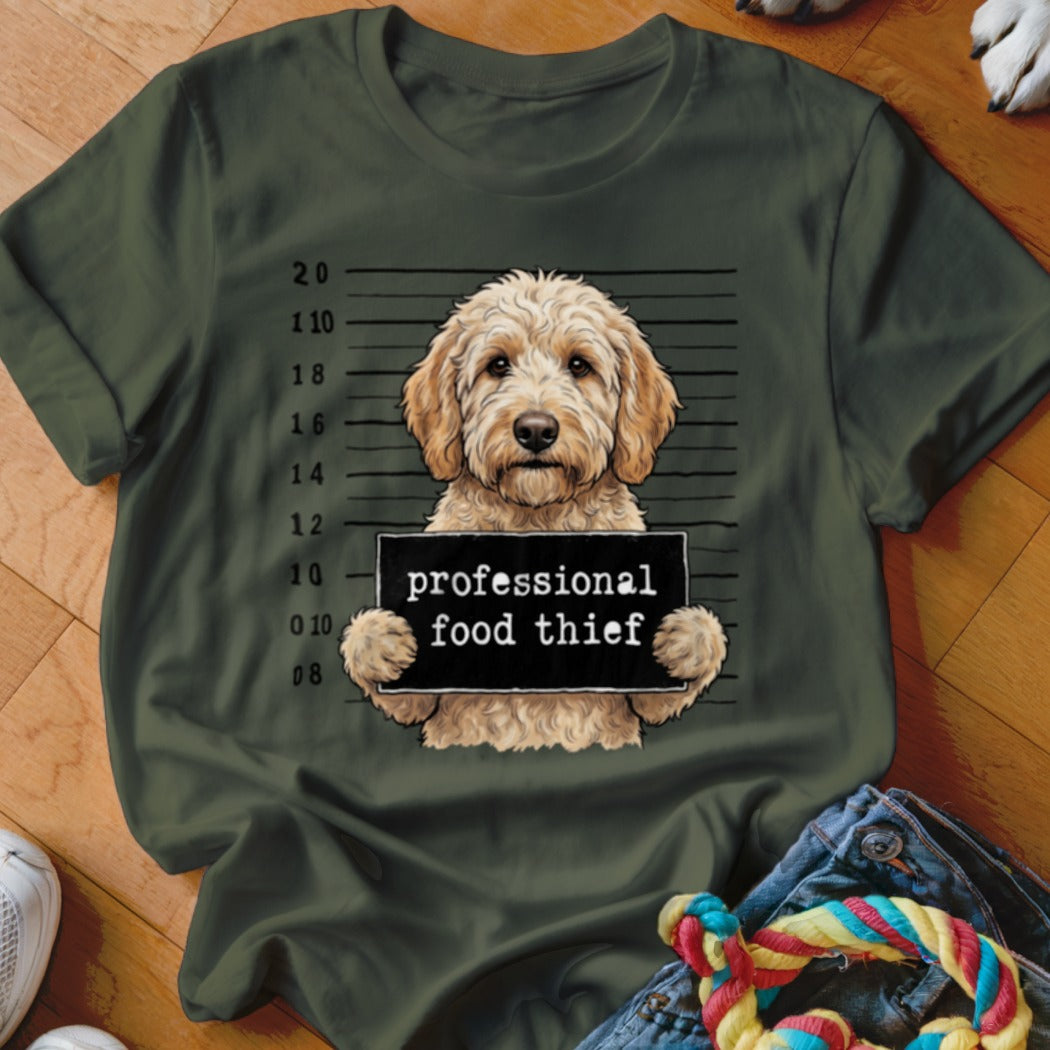Goldendoodle in mugshot holding "professional food thief" sign on a green t-shirt.