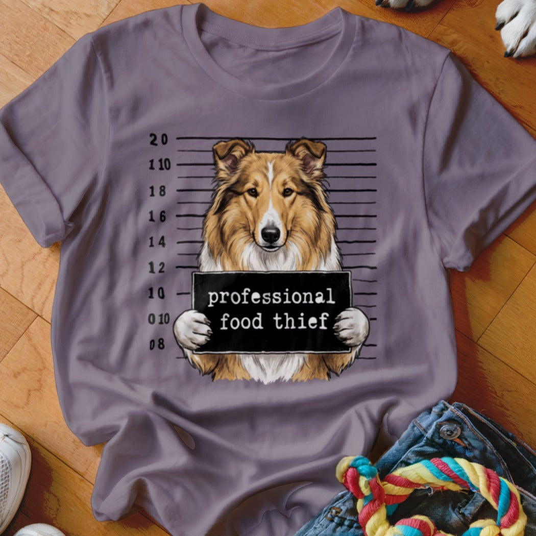 Collie dog mugshot with "professional food thief" sign on a t-shirt.