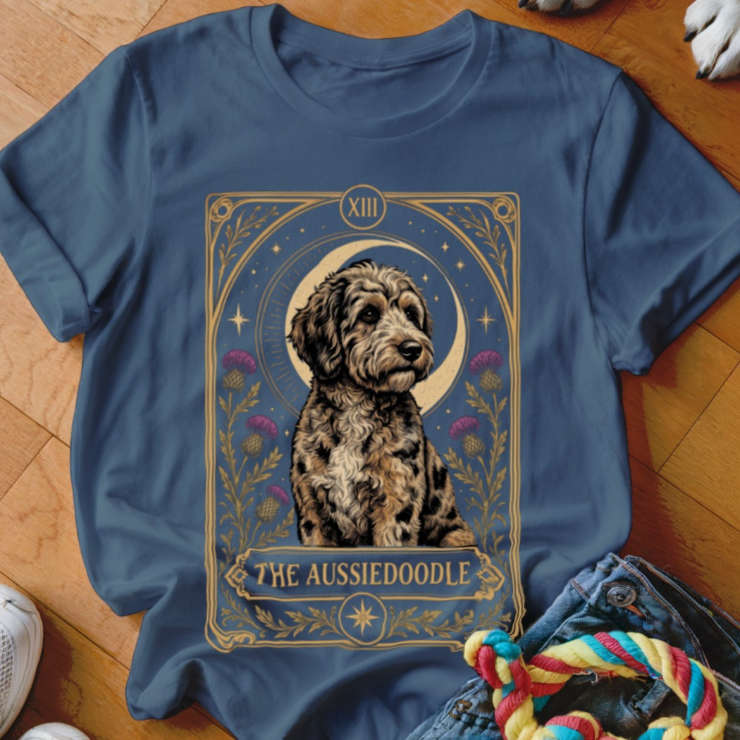 A blue crewneck t-shirt featuring a tarot card graphic of an Aussiedoodle dog, crescent moon, and purple flowers.