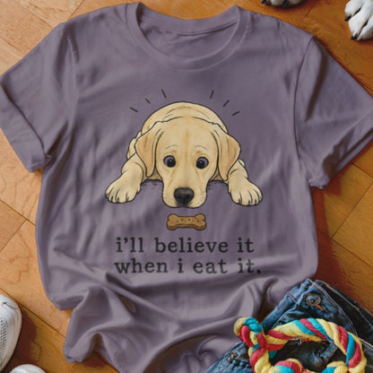 Lavender t-shirt with a cartoon of a golden retriever looking at a dog bone, text reads "I'll believe it when I eat it."