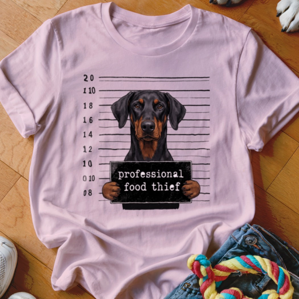 Doberman Pinscher in mugshot holding "professional food thief" sign.