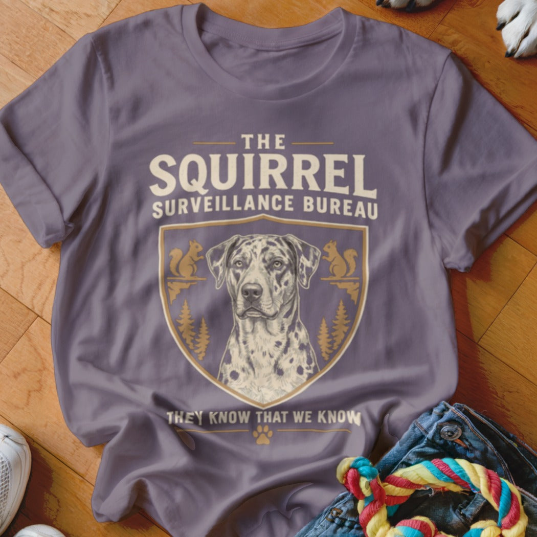 A gray t-shirt with a vintage-style graphic featuring a Dalmatian, squirrels, and text reading The Squirrel Surveillance Bureau.