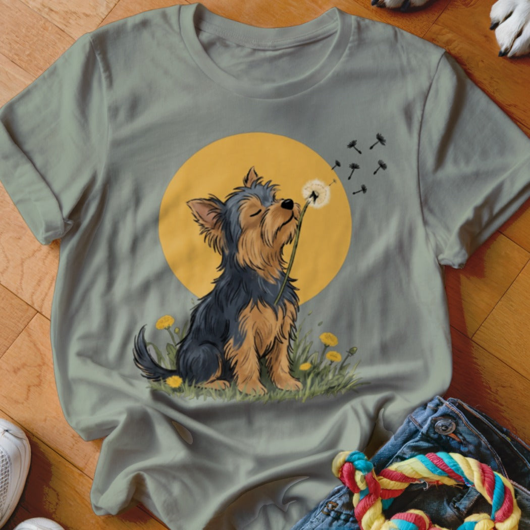 Sage green t-shirt featuring an illustration of a Yorkshire terrier blowing dandelion seeds against a yellow sun.
