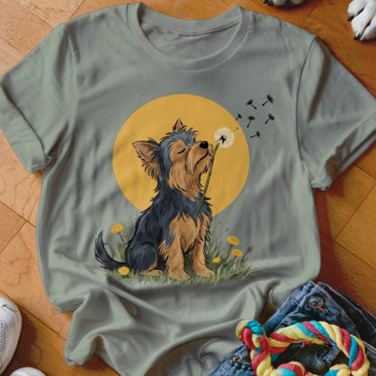 Sage green t-shirt featuring an illustration of a Yorkshire terrier blowing dandelion seeds against a yellow sun.