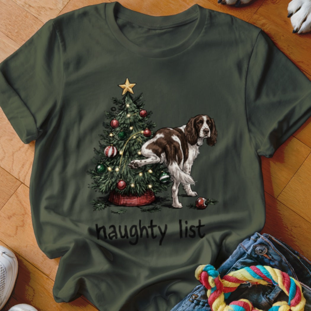 English Springer Spaniel by Christmas tree with "naughty list" text on a green t-shirt.