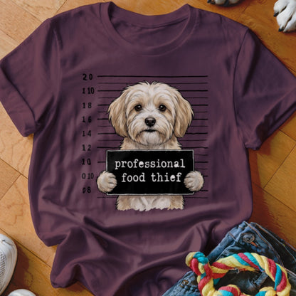 Fluffy dog holding "professional food thief" sign in mugshot style.