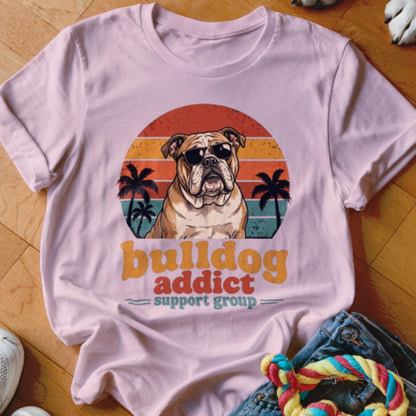 A light pink t-shirt featuring a retro graphic of an English bulldog wearing sunglasses against a sunset.