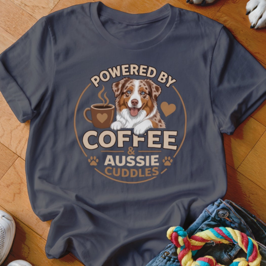 A dark gray t-shirt with a graphic of an Australian Shepherd, a coffee mug, and the text Powered by Coffee and Aussie Cuddles.