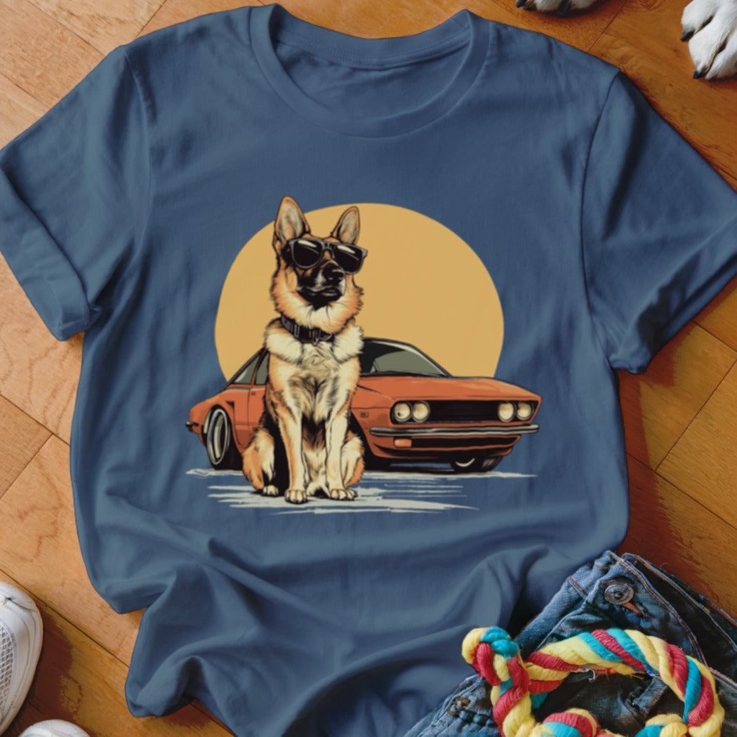 German Shepherd wearing sunglasses sitting in front of an orange car and yellow sun.