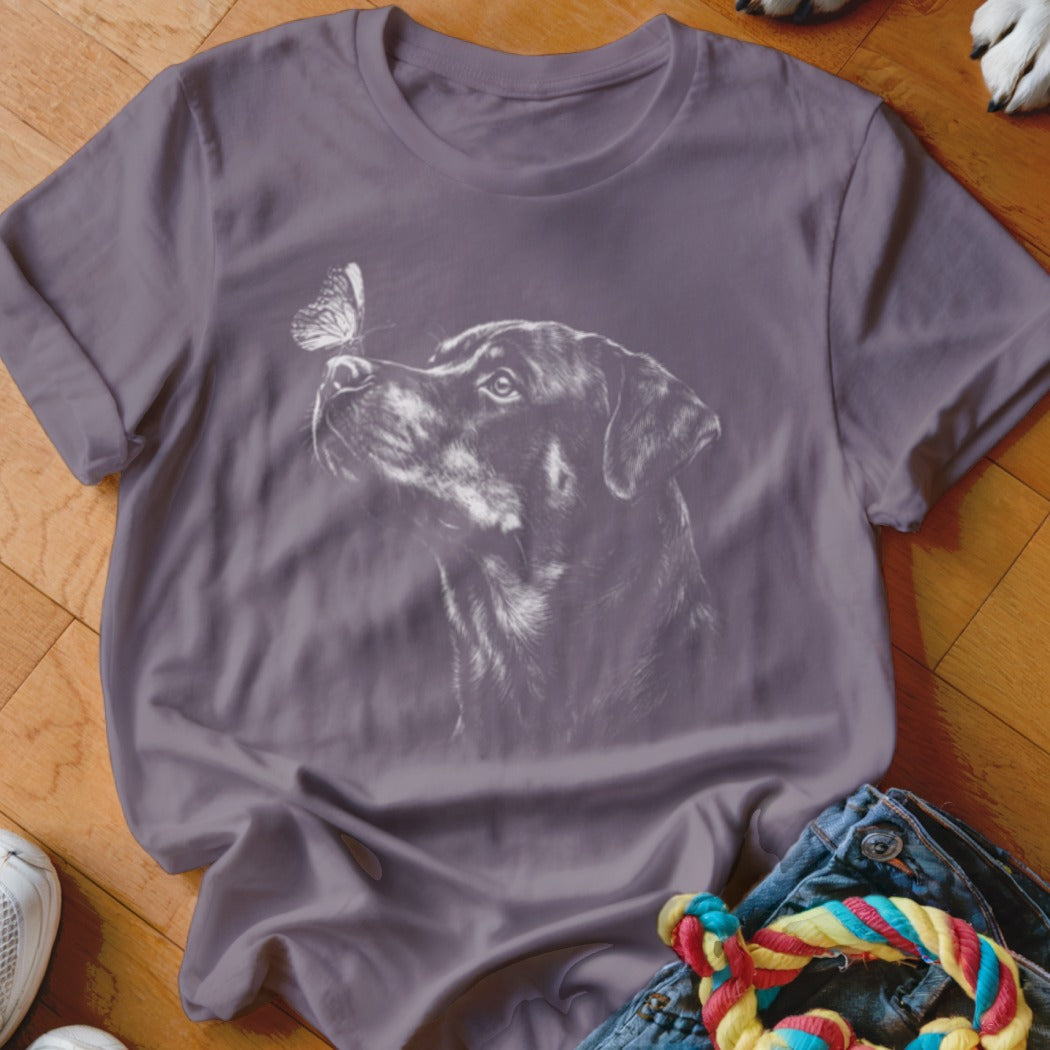 A purple short-sleeved t-shirt featuring a white graphic of a Rottweiler looking up at a butterfly.