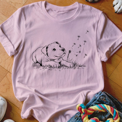 Light pink crew neck t-shirt featuring a black line drawing of a puppy blowing dandelion seeds.