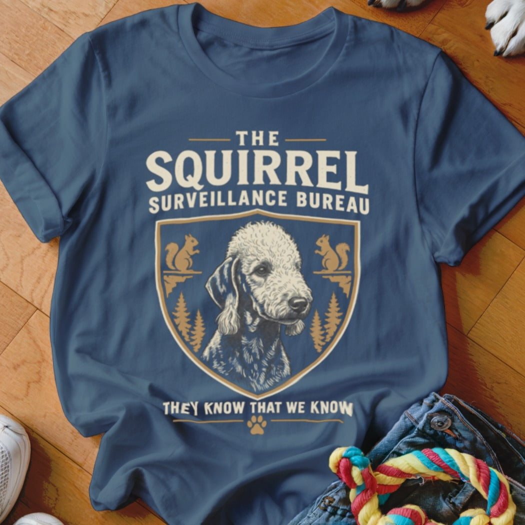 A blue crewneck t-shirt featuring the text THE SQUIRREL SURVEILLANCE BUREAU and an illustration of a dog inside a crest.