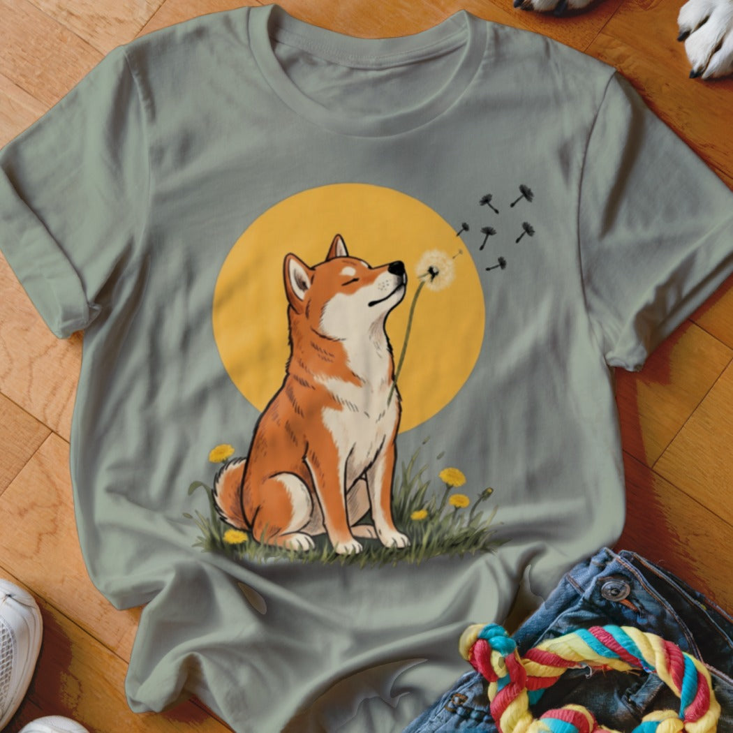 Sage green t-shirt featuring an illustration of a Shiba Inu sniffing a dandelion against a yellow circle background.