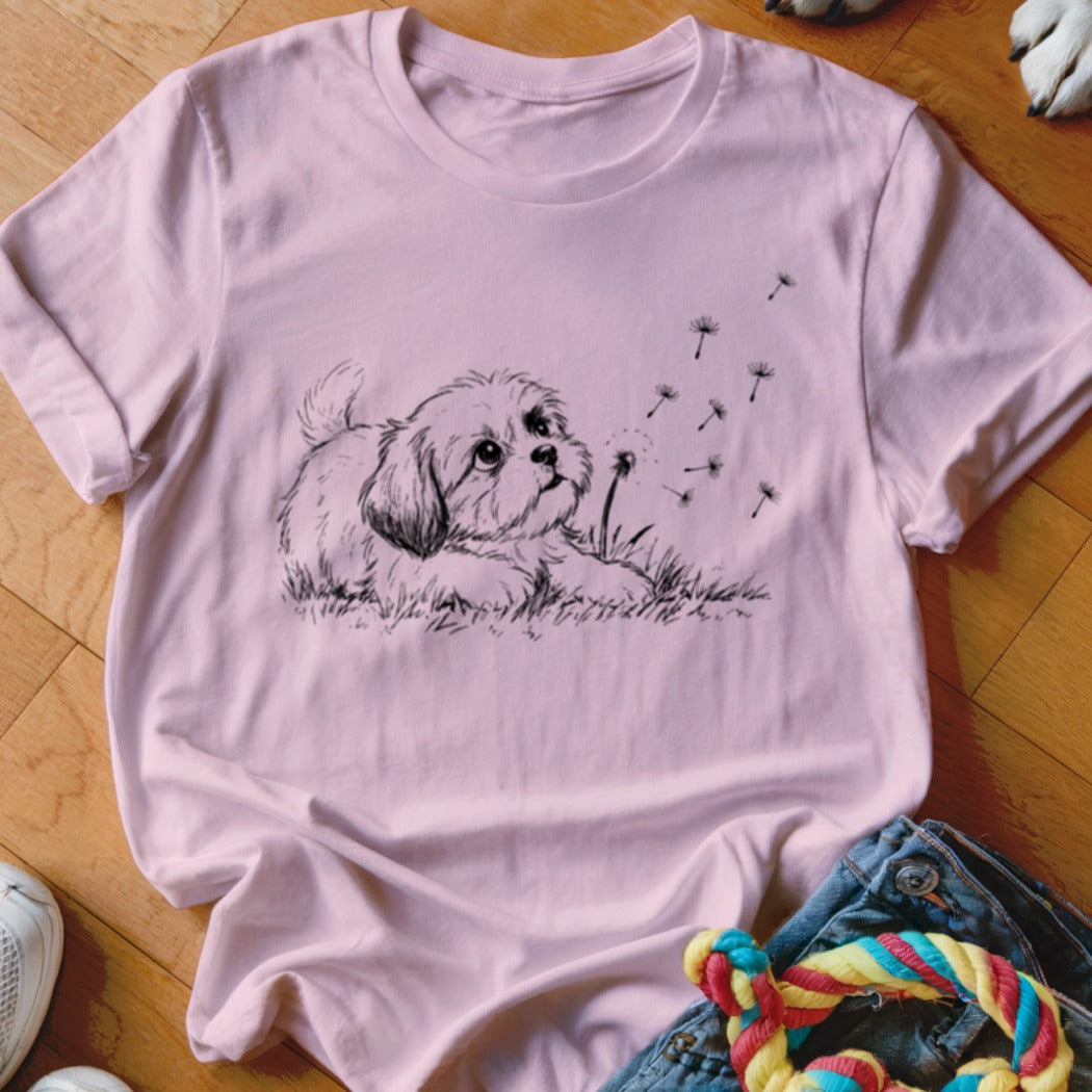 A light pink t-shirt features a black graphic of a puppy blowing dandelion seeds.
