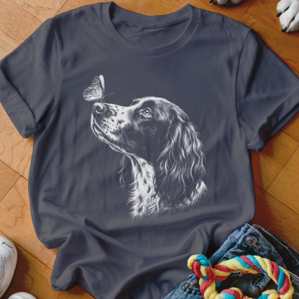 A dark grey crewneck t-shirt featuring a white sketch graphic of a spaniel dog looking at a butterfly on its nose.