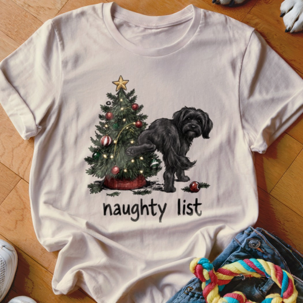 Black dog near Christmas tree with text "naughty list" on t-shirt.