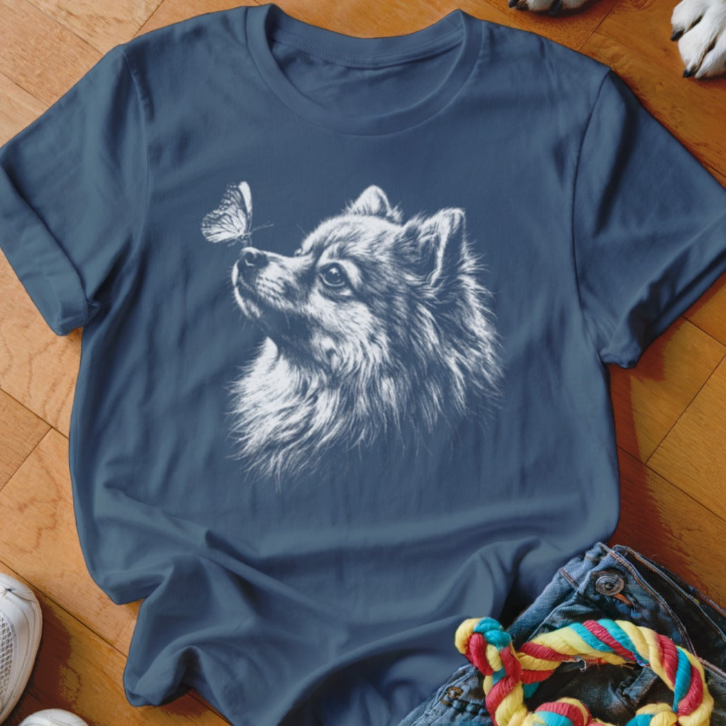 A dark blue t-shirt printed with a white sketch of a Pomeranian dog looking at a butterfly.