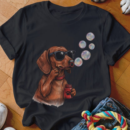 A black t-shirt featuring a graphic of a brown dachshund wearing sunglasses and blowing soap bubbles.