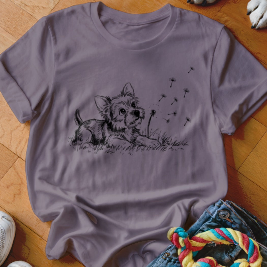 A purple t-shirt featuring a black graphic of a puppy blowing dandelion seeds.