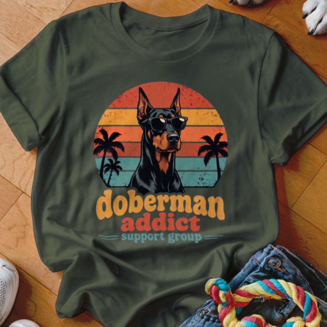 A dark green t-shirt featuring a retro graphic of a Doberman wearing sunglasses against a sunset.