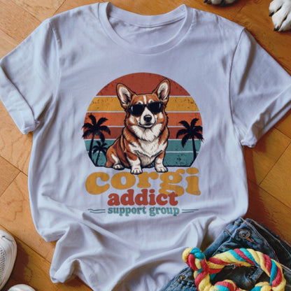 A white t-shirt featuring a corgi wearing sunglasses in front of a sunset graphic, with text reading "corgi addict support group".