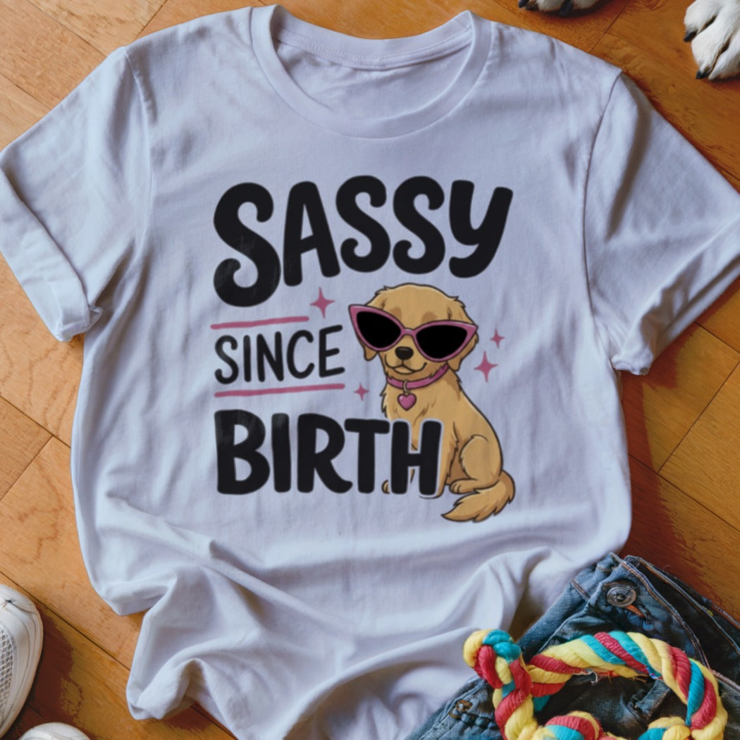 White t-shirt with cartoon golden retriever wearing sunglasses and text "SASSY SINCE BIRTH".