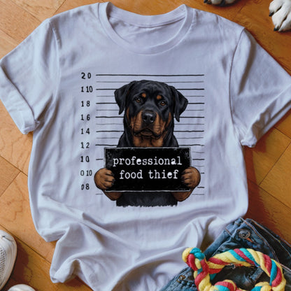 Rottweiler in mugshot holding "professional food thief" sign on white t-shirt.