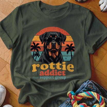 An olive green t-shirt featuring a retro graphic of a Rottweiler wearing sunglasses with palm trees and sunset background.