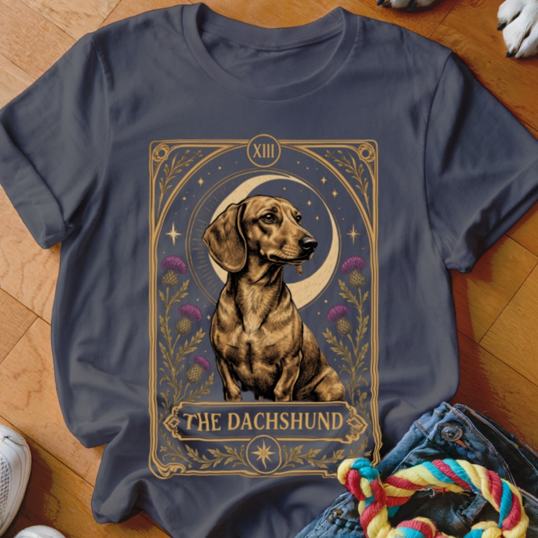 A dark gray t-shirt features a tarot card graphic of a dachshund with purple flowers, a crescent moon, and the text "THE DACHSHUND."