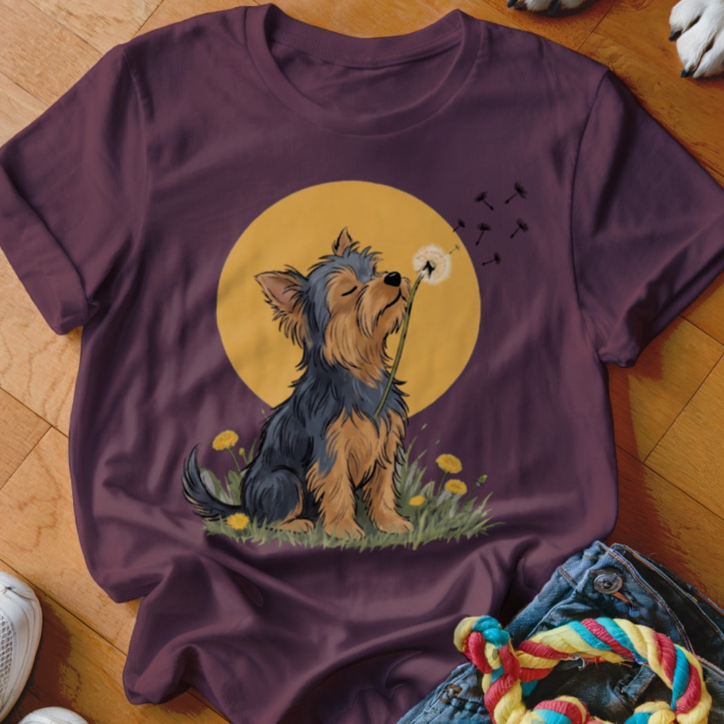 A dark purple t-shirt featuring an illustrated Yorkshire Terrier blowing a dandelion against a yellow circle background.