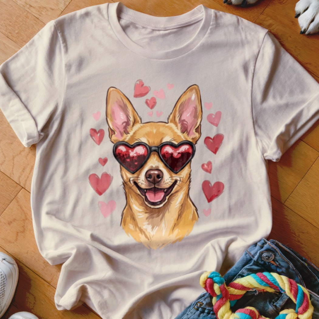 A cream-colored t-shirt with a graphic of a smiling chihuahua wearing heart-shaped sunglasses, surrounded by pink hearts.