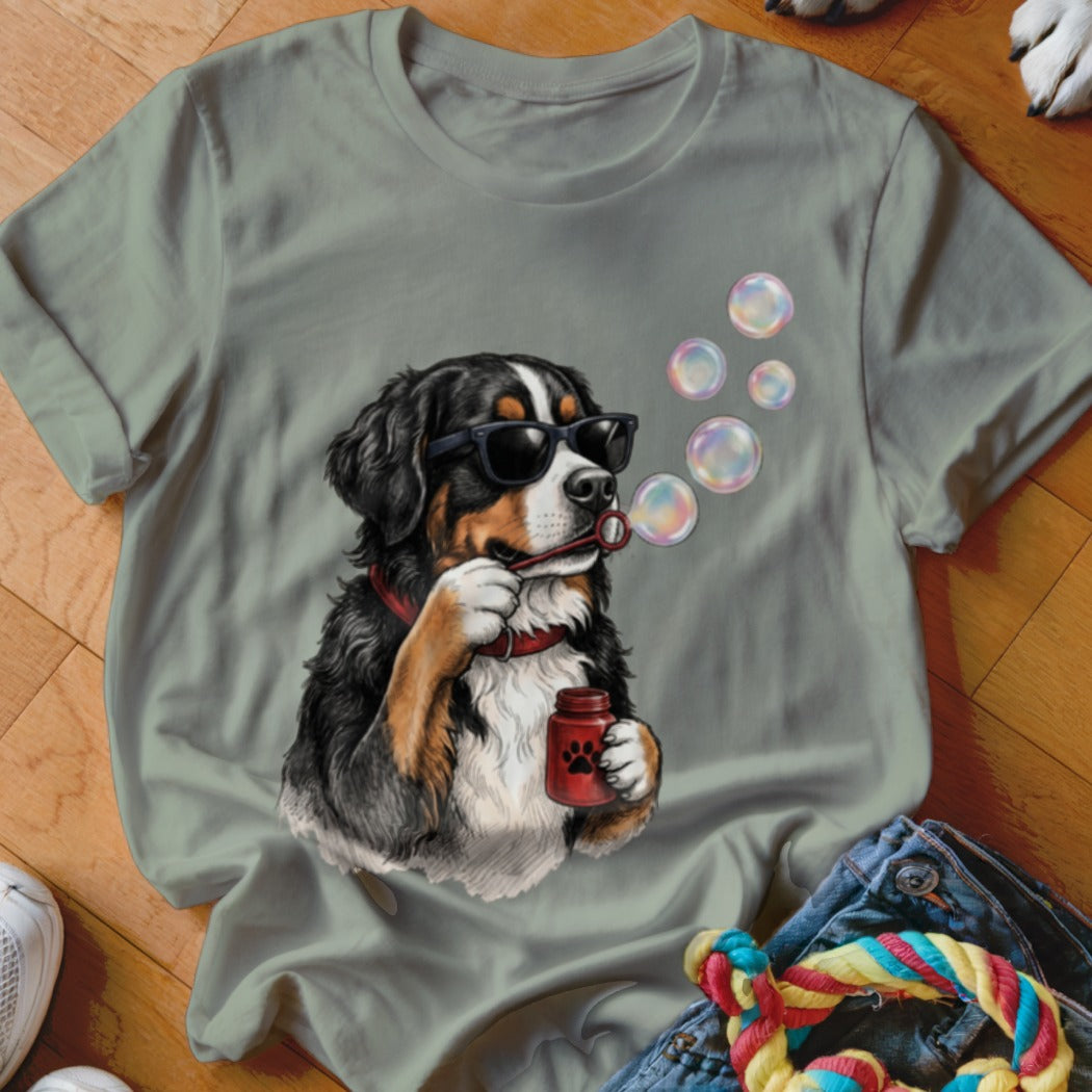 Sage green t-shirt featuring a graphic of a Bernese Mountain Dog wearing sunglasses and blowing bubbles.