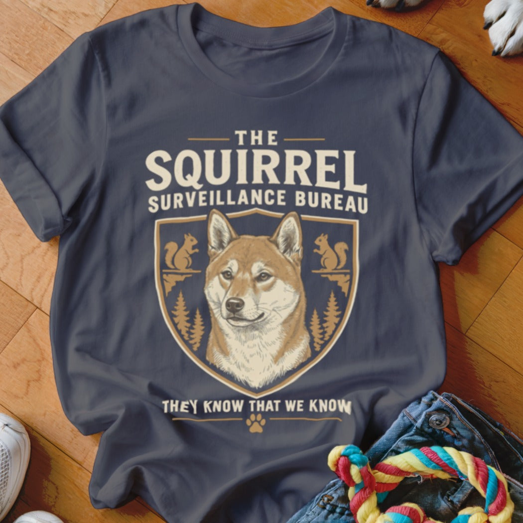 A dark gray t-shirt featuring a graphic of a Shiba Inu and text reading The Squirrel Surveillance Bureau.