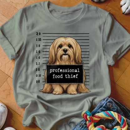 Light brown dog mugshot with "professional food thief" sign on t-shirt.