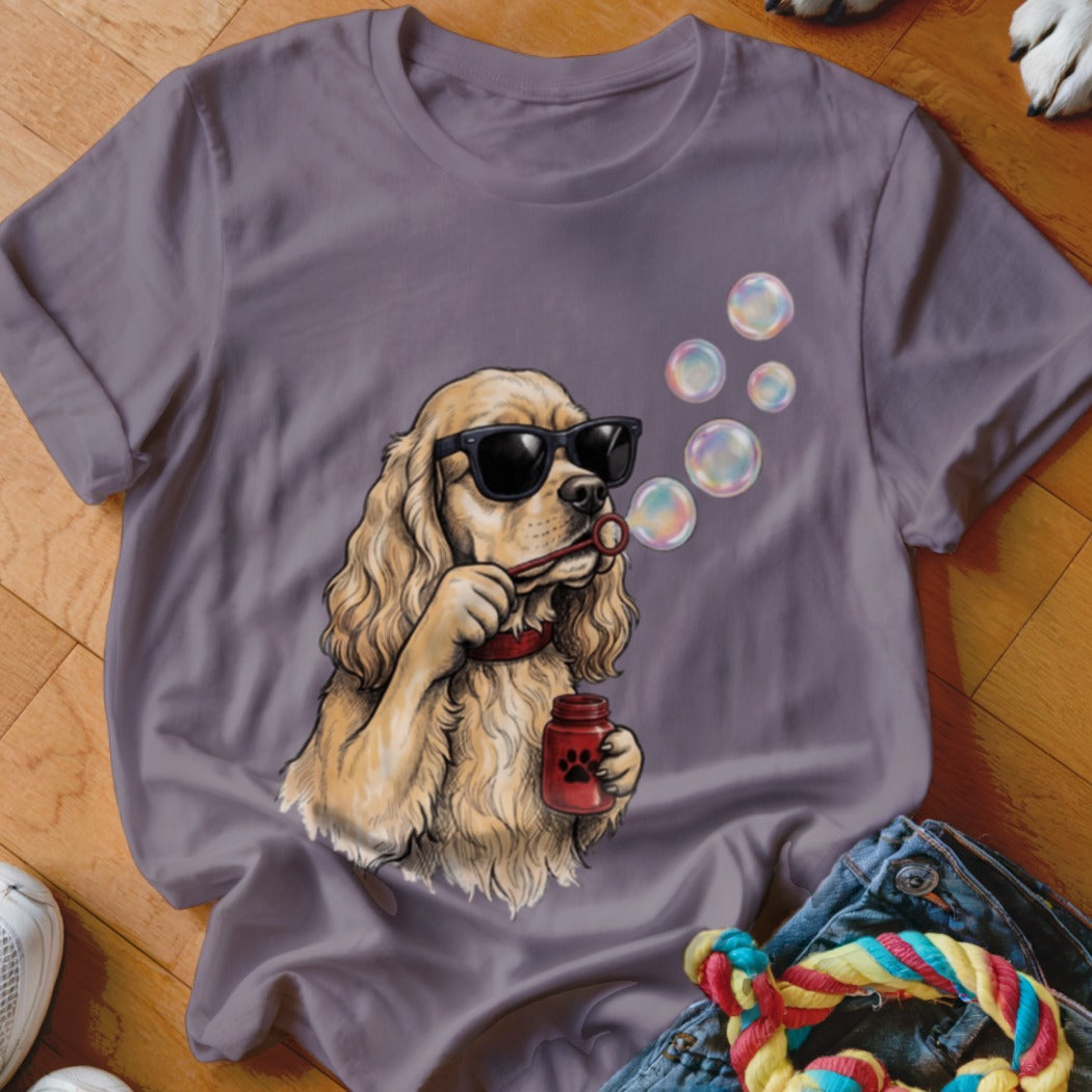 A purple t-shirt featuring an illustration of a blonde dog wearing sunglasses and blowing bubbles.
