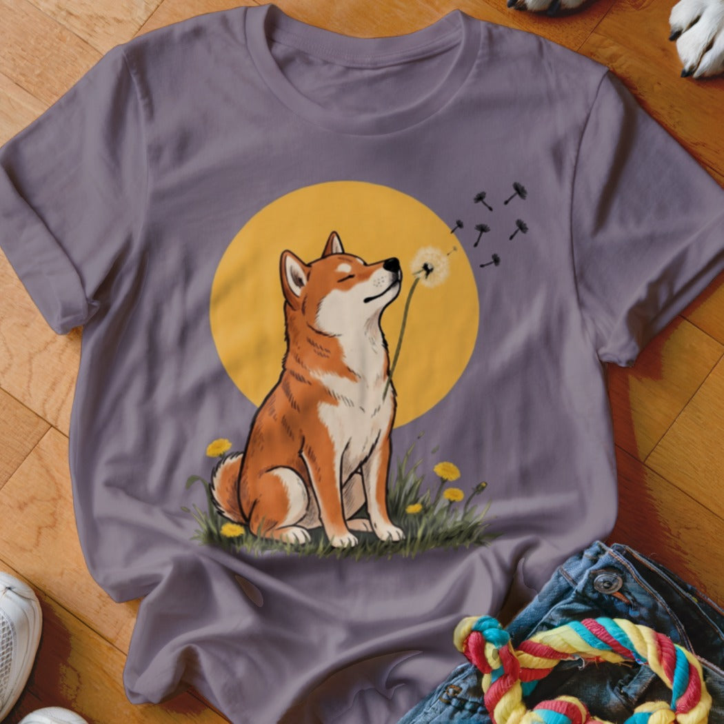 A grey t-shirt featuring a graphic of a Shiba Inu blowing dandelion seeds against a yellow circle background.